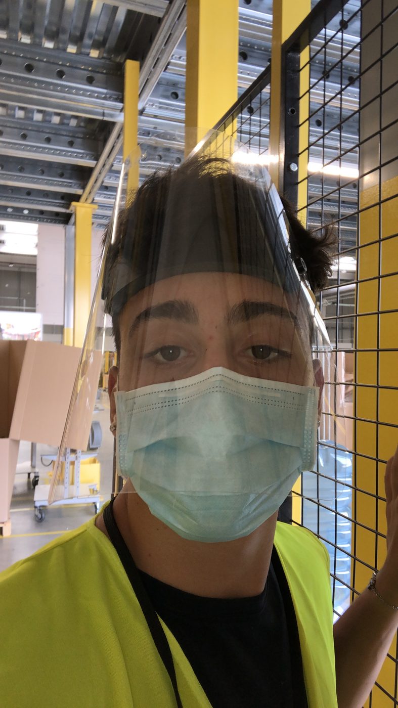 Mathias al lavoro in magazzino, con mascherina e visiera